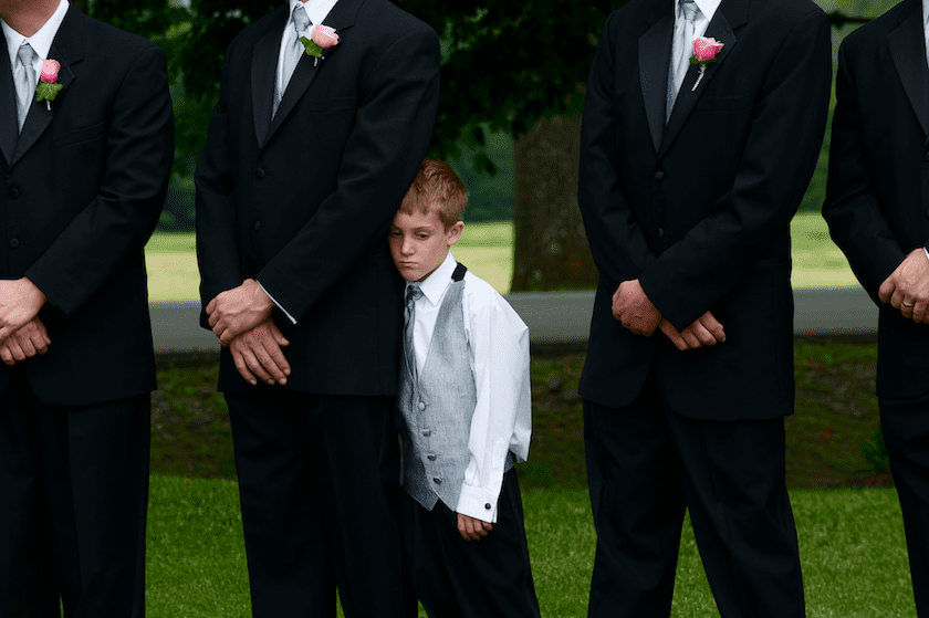 ring bearer at wedding hides behind groomsmen