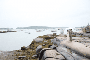 bride and groom share umbrella on the rocky ocean