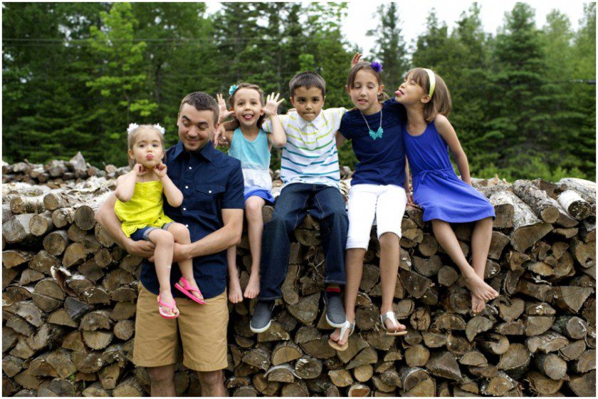 kids with dad in front of the wood pile